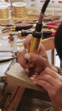 Esnaf bir kadın atölyesinde, aletler ve malzemelerle çevrili bir parça el yapımı mücevher ustalıkla hazırlıyor. Bağlılığı girişimci ruhunu yansıtıyor..