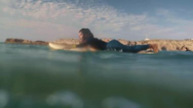 Bir kadın Taghazout, Fas 'ta gün batımında dalgalarda zarifçe sörf yapar. Altın ışık sudan yansıyarak sakin ve büyüleyici bir macera ve doğa sahnesi yaratır..