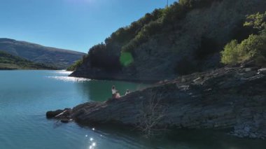 Bir kadın ve iki kızı İtalya 'nın büyüleyici doğal güzellikleriyle çevrili kayalık göl kıyılarını keşfederken hava manzarası sakin bir anı yakalıyor..
