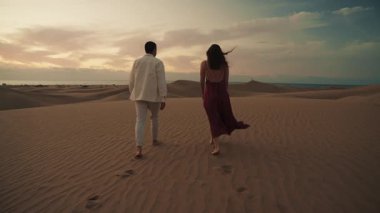 İspanya, Gran Canaria 'da gün batımında geniş bir çöl manzarasında bir çift kucaklaşır ve öpüşür. Altın kum ve uzak okyanus huzurlu ve romantik bir atmosfer yaratır. Kaçış için mükemmel..