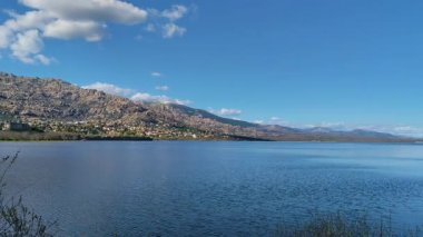 Manzanares El Real, Santillana, Madrid 'deki Guadarrama dağlarının ve sakin gölün nefes kesici manzarası. Bereketli yeşillik ve mavi gökyüzü huzurlu, resimsel bir manzara yaratır..