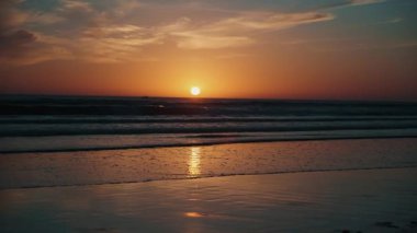 Taghazout, Fas 'ın sakin okyanus dalgaları üzerinde büyüleyici bir günbatımı. Gökyüzünü turuncu ve kırmızı renklerle boyuyor. Sakin sulara ve sakin plajlara yansıtıyor..