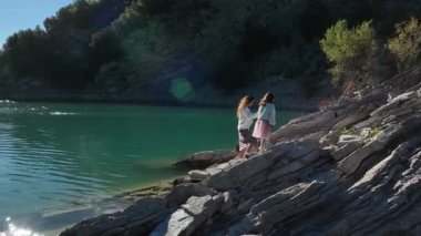 Hava aracı İtalya 'da kayalık bir göl kıyısında yürürken kızlarının elini tutan bir anneyi yakalar. Huzurlu manzara aile bağını ve doğanın güzelliğini arttırır..