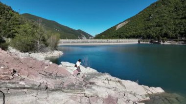 İtalya 'da kayalık bir göl kıyısında yürürken kızının elini tutan bir kadının hava görüntüsü. Canlı manzara, doğanın ve aile bağlarının güzelliğini gösteriyor..