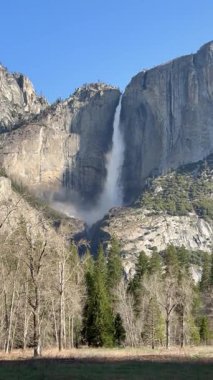 Yosemite Düşük Şelalesi 'nin sarp kayalıklardan aşağı yuvarlanışının çarpıcı manzarası. Yosemite Ulusal Parkı, Kaliforniya' da yemyeşil ve açık mavi gökyüzü ile çevrili..