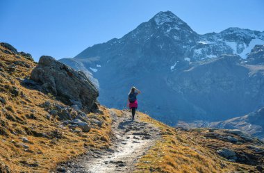 Sırt çantalı genç bir kadın İsviçre Alplerinde kayalık dağ yolunda yürüyüş yapıyor. Yüksek dağların manzarası, kızım, engebeli manzarası ve açık gökyüzü. Yürüyüş, macera ve doğa yolculuğu kavramı