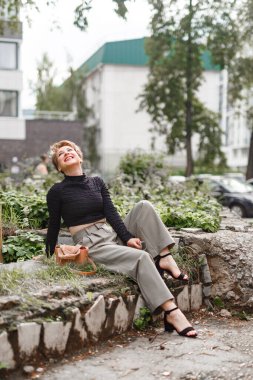 Neşeli orta yaşlı bir kadın yeşil bir şehir parkında huzur içinde dinleniyor. Keyifli bir günde temiz hava ve doğal çevreyi izlerken mutlu bir şekilde gülümsüyor..