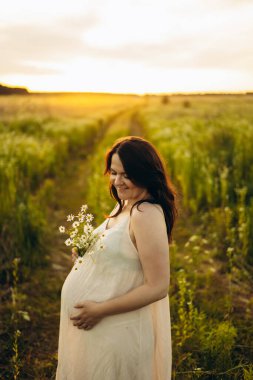 Huzurlu bir çayırda hamile bir kadının, huzurlu bir gün batımı yürüyüşünün tadını çıkarması, karnını kucaklaması ve kır çiçeklerini tutması, umudu, aşkı ve annelik beklentisini simgeliyor..