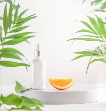 Kozmetik pipet şişesi ve turuncu dilim yeşil tropikal yapraklarla beyaz arka planda podyumda. C vitamini serumu. Modern cilt bakımı ve güzellik ürünlerinin sunumu