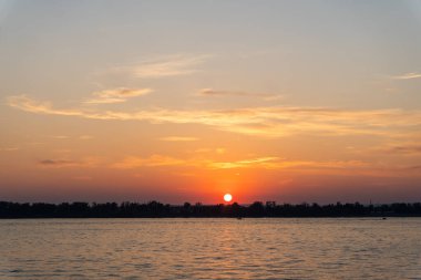 Huzurlu bir nehir manzarasında nefes kesici bir gün batımı. Güneş, suyun yüzeyine yansıyan ılık bir parıltı yayar. Huzurlu ve sakin bir atmosfer yaratır..