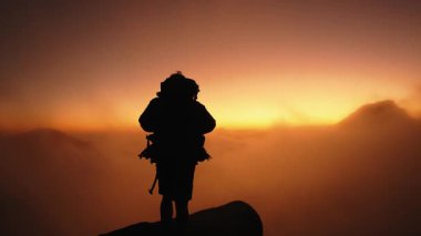 Yalnız bir maceracı Madeira 'da bir zirvenin tepesinde duruyor, nefes kesici bir gün doğumuna karşı silueti var. Altın renkler ve yuvarlanan bulutlar çarpıcı, sakin bir manzara yaratır..