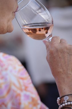 Kadın bir bardak gül şarabının tadını çıkarıyor, sosyete toplantısında aromanın ve aromanın tadını çıkarıyor.