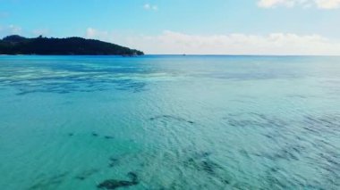 Yazın Seyşeller sahilinin nefes kesici güzelliği, berrak mavi gökyüzünün altında sakin bir turkuaz okyanus ve uzak yemyeşil tepeler, huzurlu bir cennet yaratıyor..