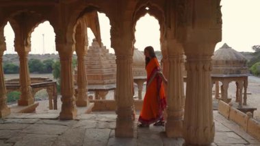 Geleneksel giysiler içindeki bir kadın, antik bir Hint tapınağının karmaşık mimarisine hayran. Güzel taş oymalar, tarihi detaylar ve kültürel önem barındırıyor..
