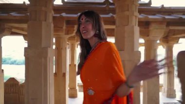 Geleneksel turuncu sari giyen bir kadın, antik bir Hint tapınağını keşfediyor. Kültürel özünü ve mimari güzelliğini büyüleyici bir turist olarak yakalıyor..