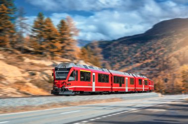 Kızıl modern yolcu treni sonbaharda günbatımında İsviçre Alplerinde demiryolunda hareket ediyor. Dağlarda, yolda yüksek hız treni hareket bulanıklığı ile sonbaharda portakal ağaçları. Bernina Ekspresi, İsviçre