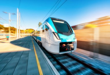 Yüksek hızlı mavi yolcu treni gün batımında tren istasyonunda hareket ediyor. Tren istasyonu. Hareket bulanıklığı olan modern demiryolu taşımacılığı konsepti. Demiryolu. Slovenya 'da ticari ulaşım