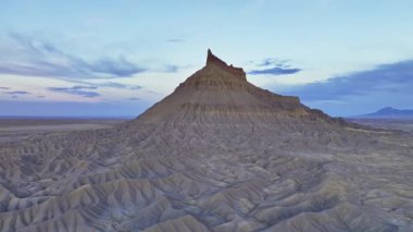 Utah, ABD 'deki Fabrika Butte' ı çevreleyen dramatik ve engebeli manzaraların hava görüntüsü, alacakaranlıkta gökyüzünde yumuşak pastel renklerle çekilmiş, eşsiz jeolojik oluşumlarını vurguluyor..