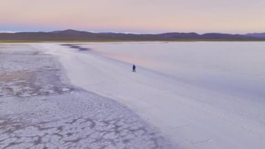 Tek başına bir adam Salinas Grandes 'in engin, sakin genişliğinde yürür şafak vakti Arjantin, Salta' da, ufuk çizgisi ve arka planda uzak dağlarla.
