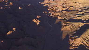 Arjantin, La Puna 'nın çarpıcı yüksek irtifa manzarası boyunca uzanan ıssız bir çöl yolunun havadan görünüşü. Gölgeler kurak arazi boyunca uzanıyor, eşsiz topoğrafyayı vurguluyor..