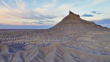 Utah 'taki Fabrika Butte' ın görkemli manzarası engebeli arazisini ve renkli günbatımı gökyüzü altında eşsiz jeolojik özelliklerini sergiliyor. Doğanın sanatını yansıtan mükemmel bir sahne..