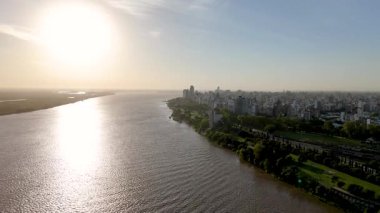 Günbatımının altında parlayan Parana Nehri 'nin havadan görünüşü, Rosario şehrinin ufuk çizgisi yemyeşil bankalar boyunca uzanıyor, modern şehir mimarisini gözler önüne seriyor..