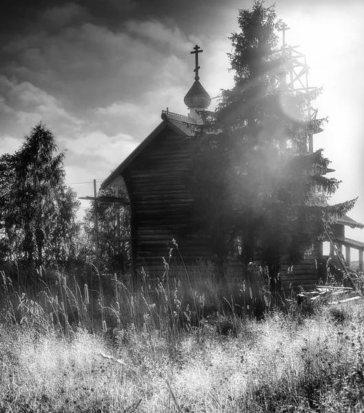 Houten orthodoxe kapel in het hoge gras. Een warme zomerdag. Achtergrondverlichting. Bewolkte hemel. Zwart-wit beeld. — Stockfoto