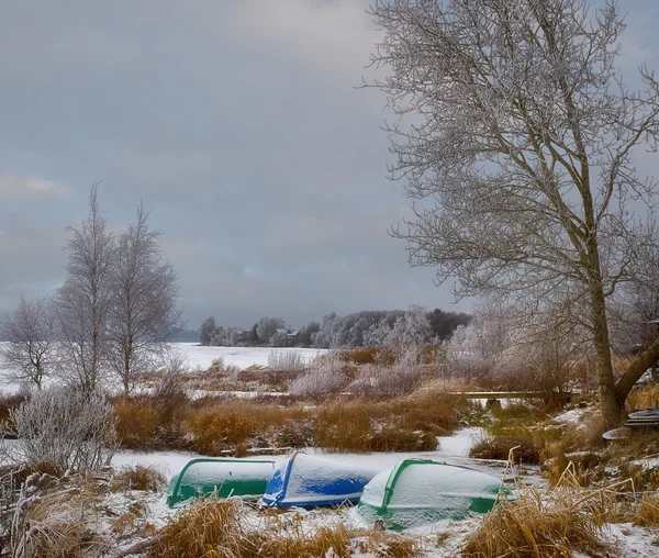 Beginning of winter. Boats on the shore of a frozen lake. Early morning. Yellow grass and snow.