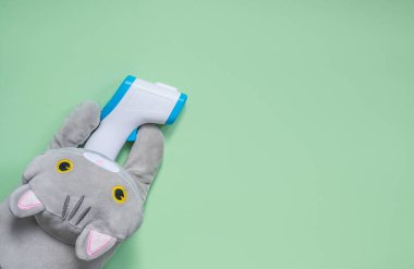 Güzel bir kedi yavrusunu kapatın ve yeşil arka plan manzaralı bir kızılötesi cihazla sıcaklığı ölçün. Çocuk hastanesi.