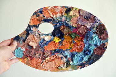 Beyaz arka planda sanat paletine yakın plan. Yağlı boyaların parlak noktaları. kullanılmış palet. çok renkli boyalar var. Metne yer var..