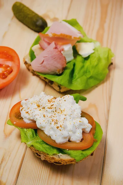 Closeup of homemade sandwich with ham, cottage cheese, fresh tomato and green salad on wooden table