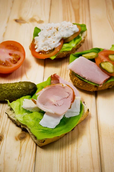 Closeup of homemade sandwich with ham, cottage cheese, fresh tomato and green salad on wooden table