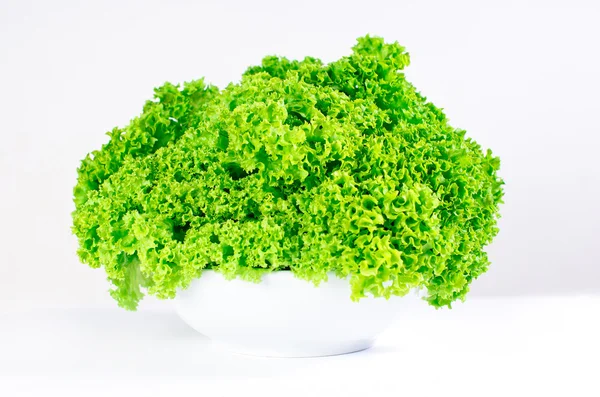 Corrugated leaves of fresh vegetable salad in white bowl on white table