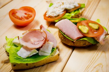 Closeup of homemade sandwich with ham, cottage cheese, fresh tomato and green salad on wooden table