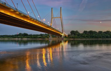 Backlit bridge at night and reflected in the water.Siekierkowski bridge