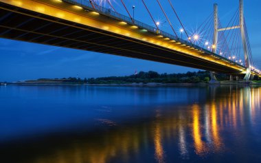 Backlit bridge at night and reflected in the water.Siekierkowski bridge