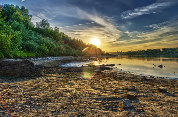 Canoe and paddles beached on shore. Sunset near river