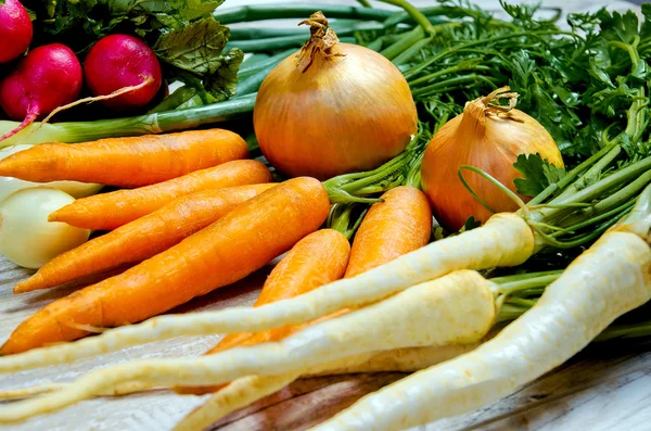 Verduras jóvenes de primavera sobre fondo de madera. Las zanahorias, el rábano, el perejil, la cebolla - la cosecha fresca del jardín — Foto de Stock