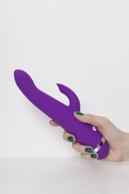 Violet dildo in the woman's hand on a white background with room for text. Vibrator and masturbation. Sex shop