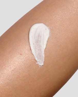 Bir kadın derisinin derisinden deri yüzen vücut fırçasıyla yakın çekim makro görüntüsü. Görünür parçacıklara sahip kremsi beyaz doku cilt bakımını ve güzellik kavramlarını ön plana çıkarır. Görüntü kendine özgüveni, vücut derisini ve pürüzsüz cildi temsil ediyor..