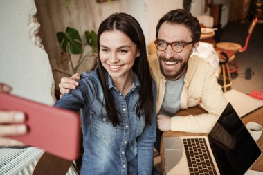 Kafede laptopun yanında bir adamla selfie çeken mutlu bir kadın.