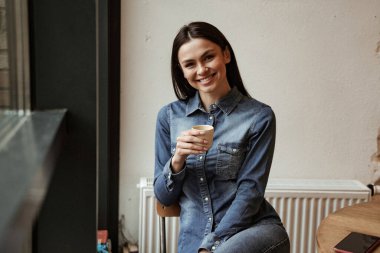 Akıllı telefonun yanında elinde bir fincan kahve tutan neşeli bir kadın.