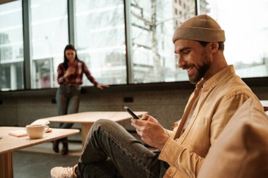 Kafedeki koltukta otururken akıllı telefondan mesaj atan neşeli bir adam.