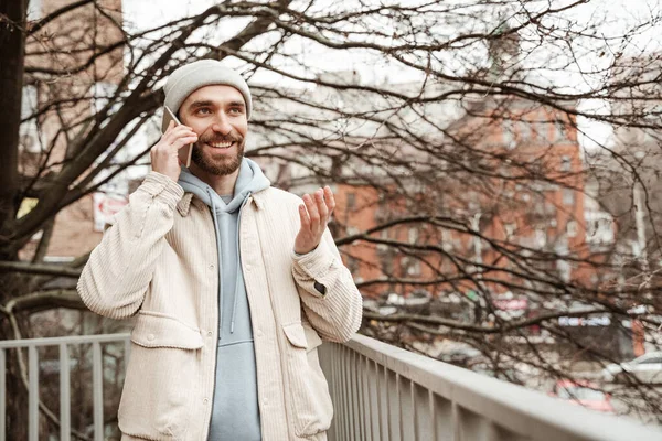 happy bearded man in beanie hat talking on smartphone