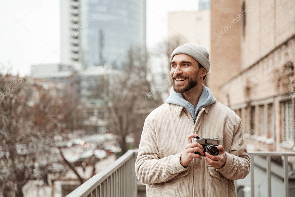 bearded man in beanie hat and jacket smiling while holding retro camera 