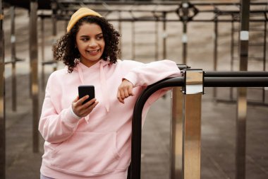 Mutlu Afro-Amerikan kadın spor giyim sektöründe akıllı telefondan sohbet ederken gözlerini kaçırıyor.