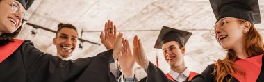 Mezuniyet sınıfı 2021 'de elinde diploma ve şapkalı mutlu ırklar arası öğrenciler beşlik çakıyor.
