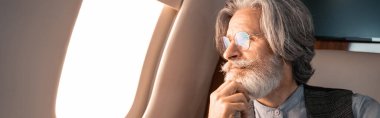 Mature man in eyeglasses looking at airplane window, banner  clipart