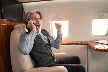 Heyecanlı iş adamı özel uçakta gözlük yanında akıllı telefondan konuşuyor. 