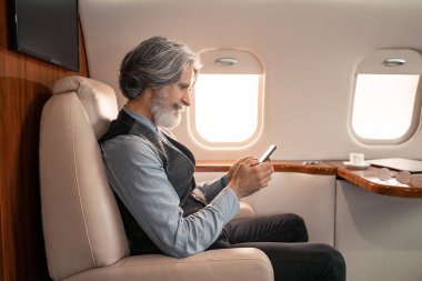Yetişkin bir iş adamının gözlük yanında akıllı telefon kullanması ve jette bulanık bardak kullanması. 